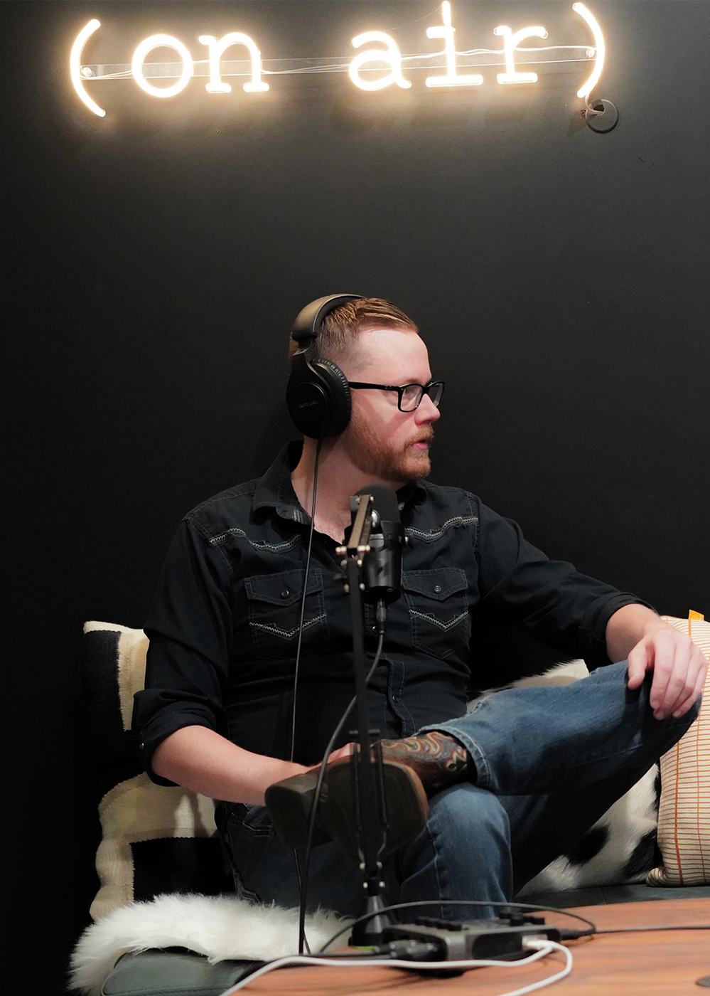 A podcast host at the microphone under an on-air neon sign